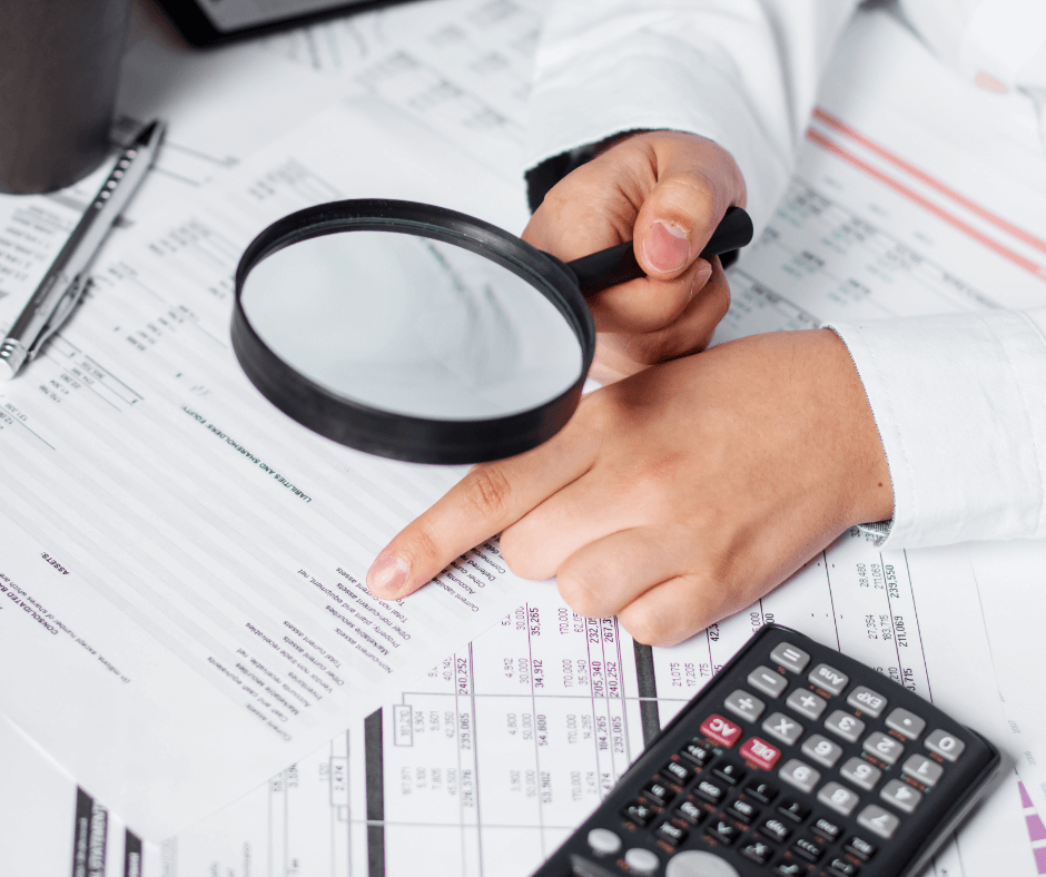 Un comptable infirmier libéral examinant attentivement des documents financiers avec une loupe, indiquant une analyse méticuleuse des détails comptables spécifiques à la pratique infirmière en libéral.